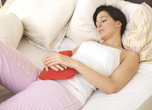 Woman with hot water bottle over her abdomen for menstrual discomfort.