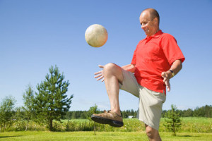 Older male hitting soccer ball with his knee.